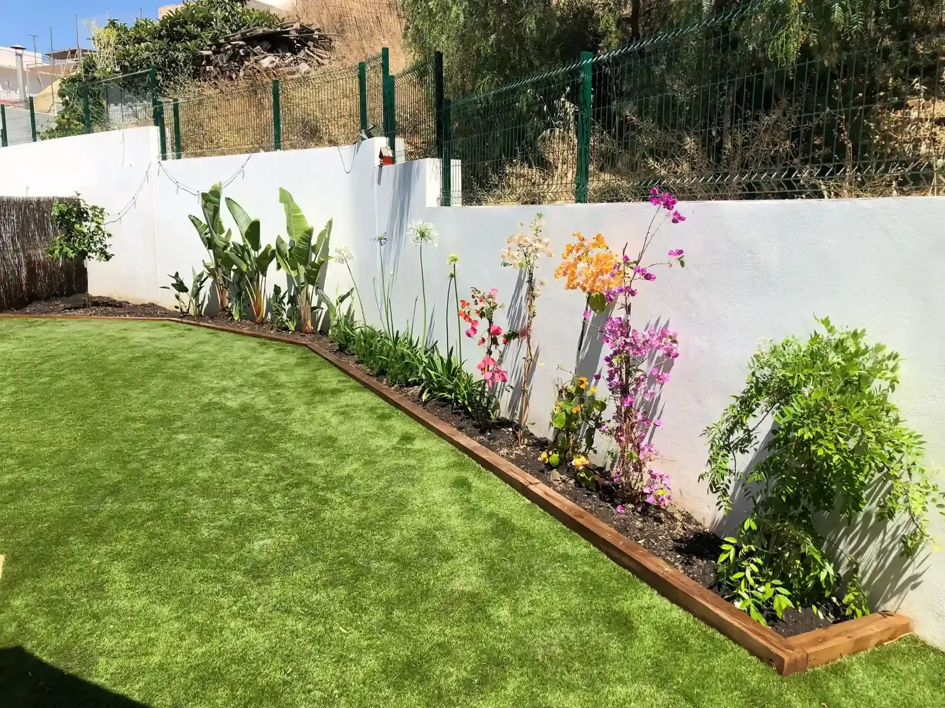 Un exuberante césped verde bordea una pared blanca adornada con coloridas flores y plantas.