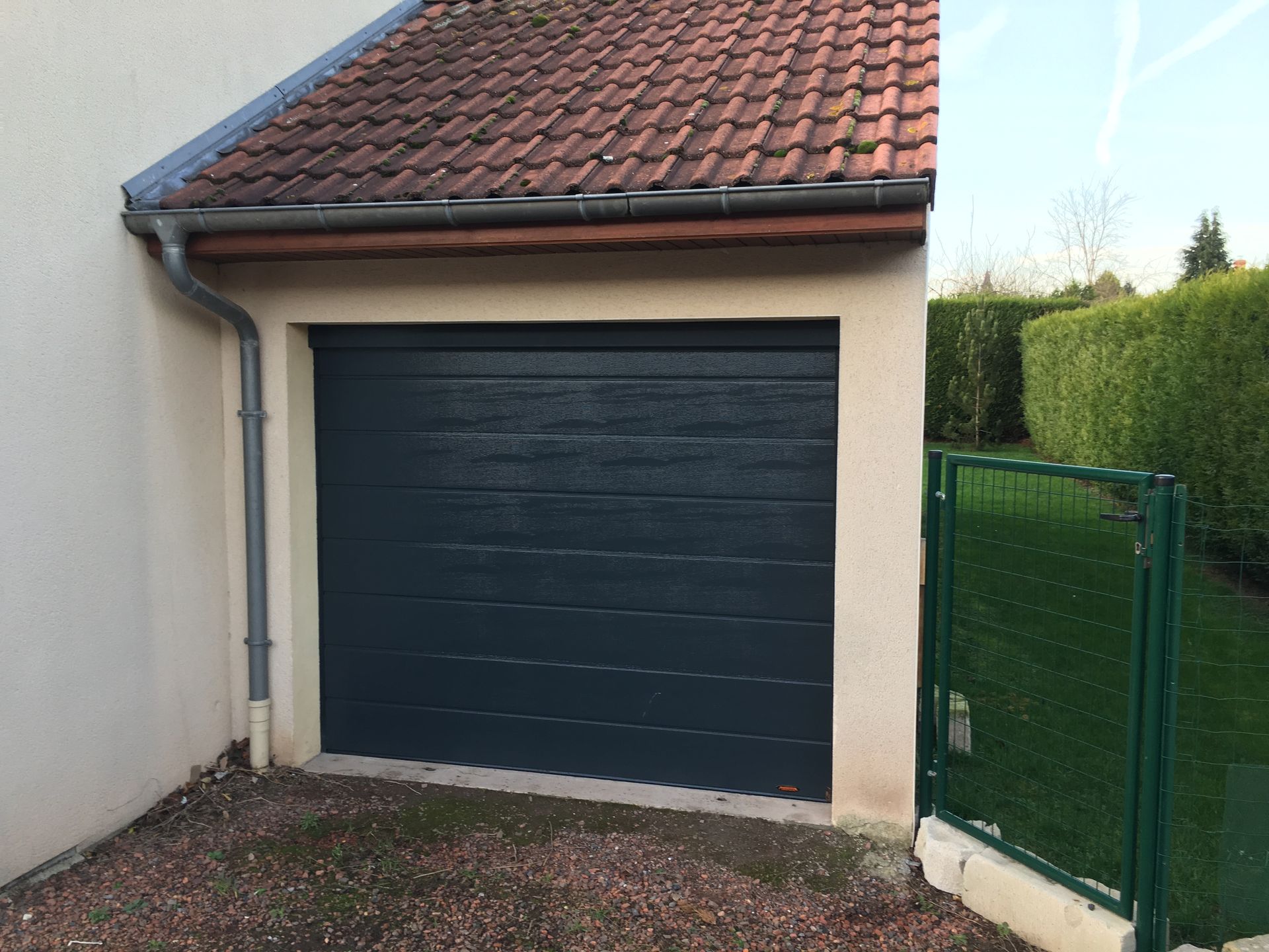 Garage avec porte bleu foncé et toit de tuiles rouges.