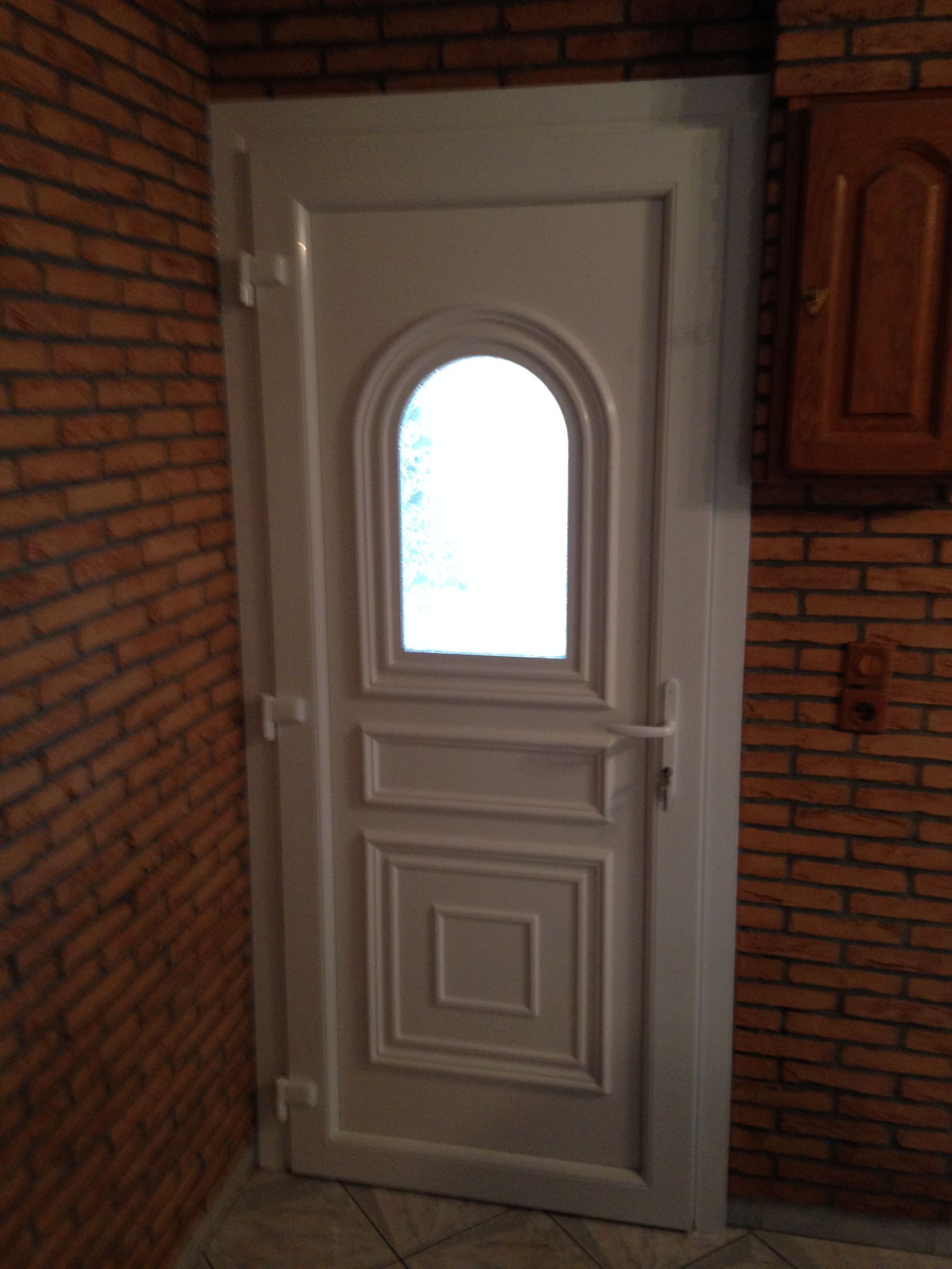 Porte blanche avec fenêtre cintrée, sur un mur de briques.