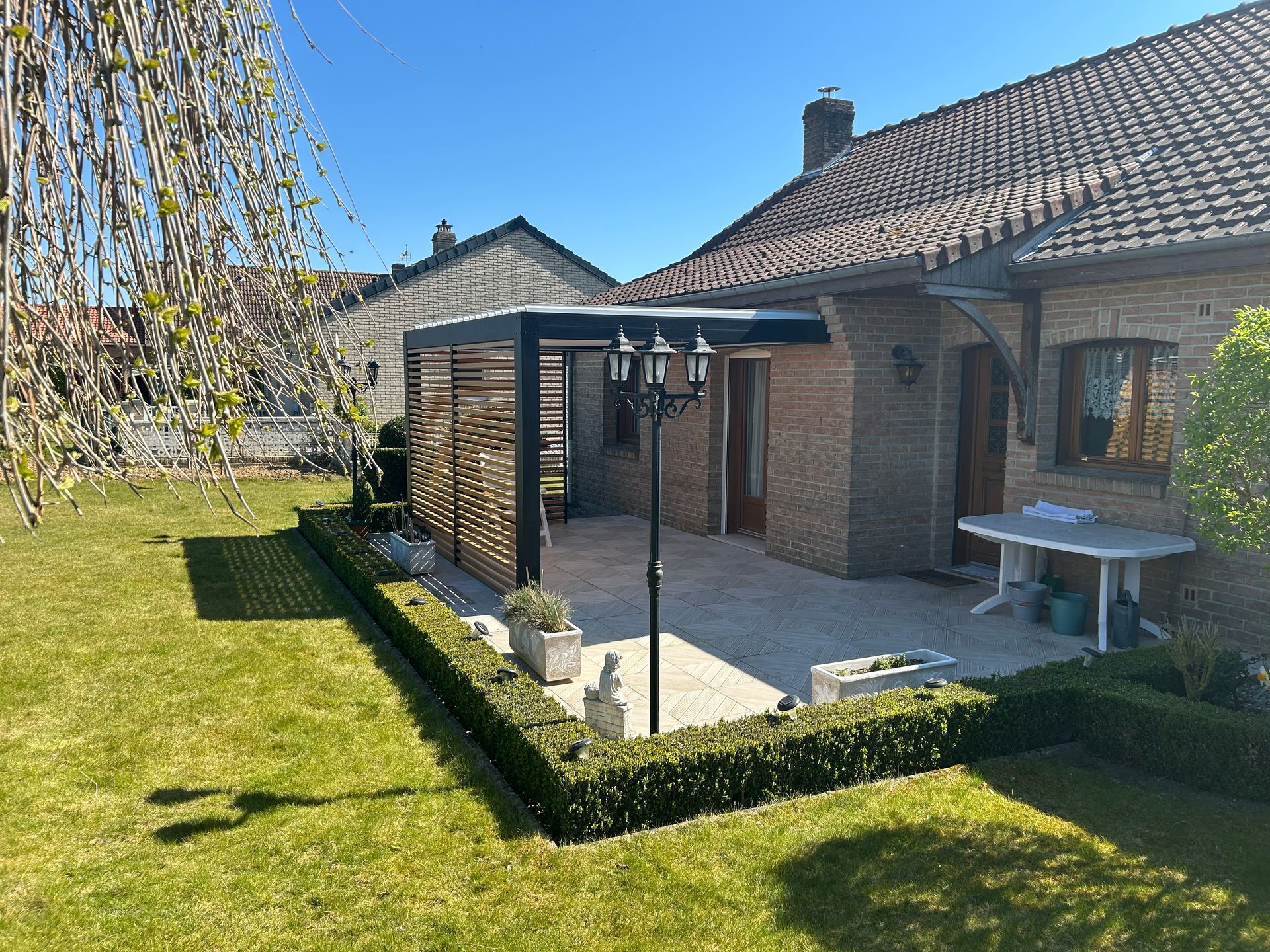 Pergola noire, maison en briques et pelouse verte.