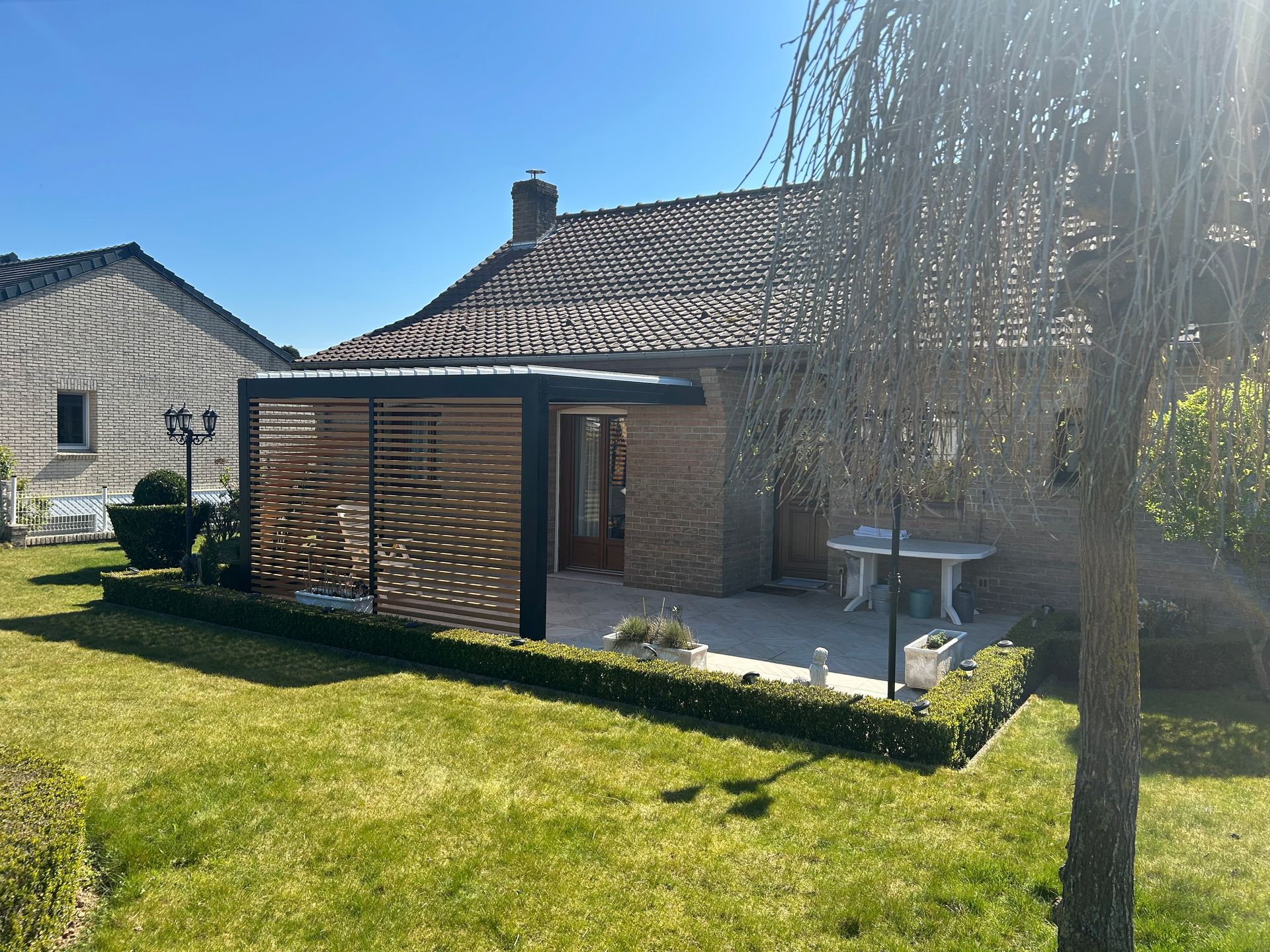 Extérieur de la maison avec une pergola en bois, une façade en briques et une pelouse.
