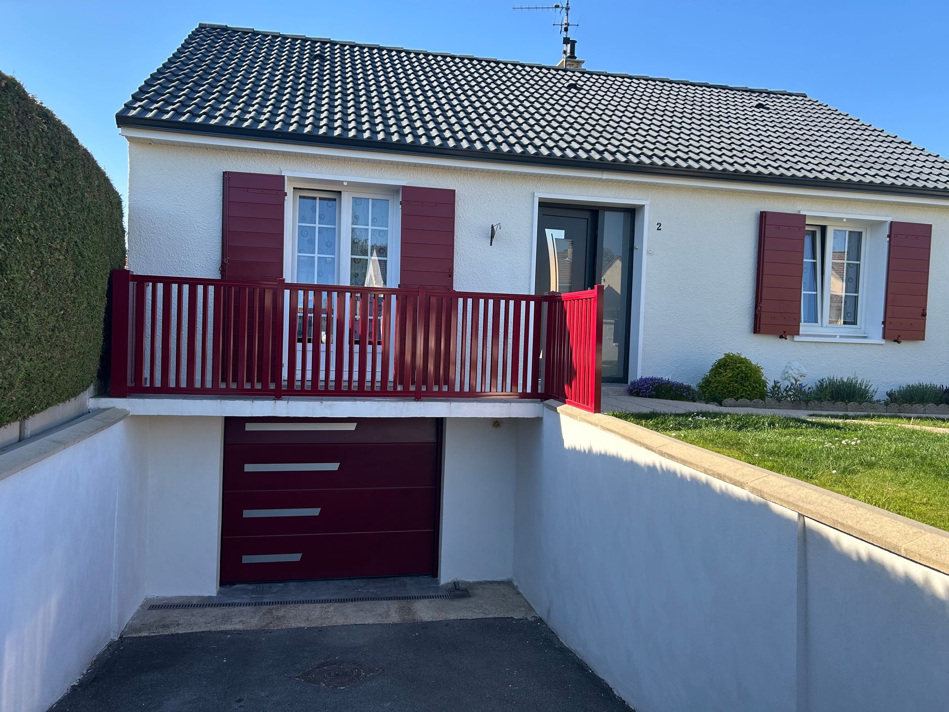 Maison blanche avec volets rouges, garde-corps et porte de garage.