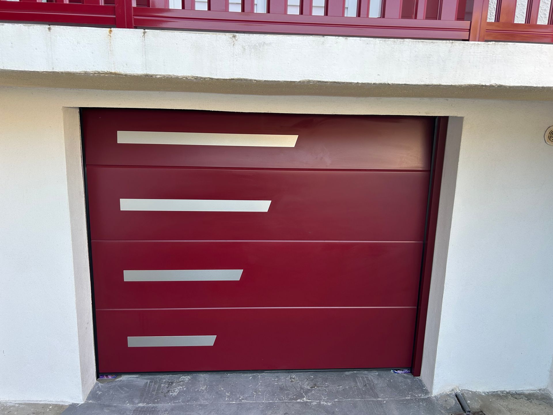 Porte de garage bordeaux avec des accents argentés horizontaux.