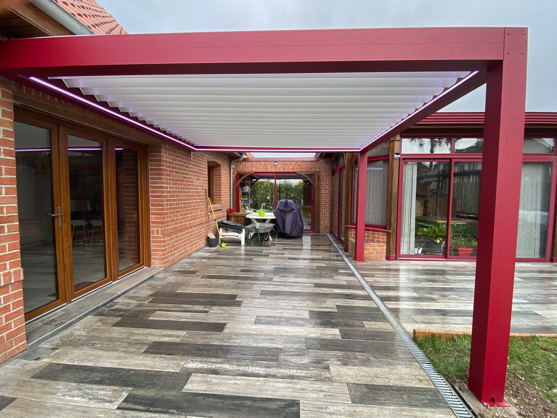 Pergola rouge surplombant une terrasse en pierre humide.