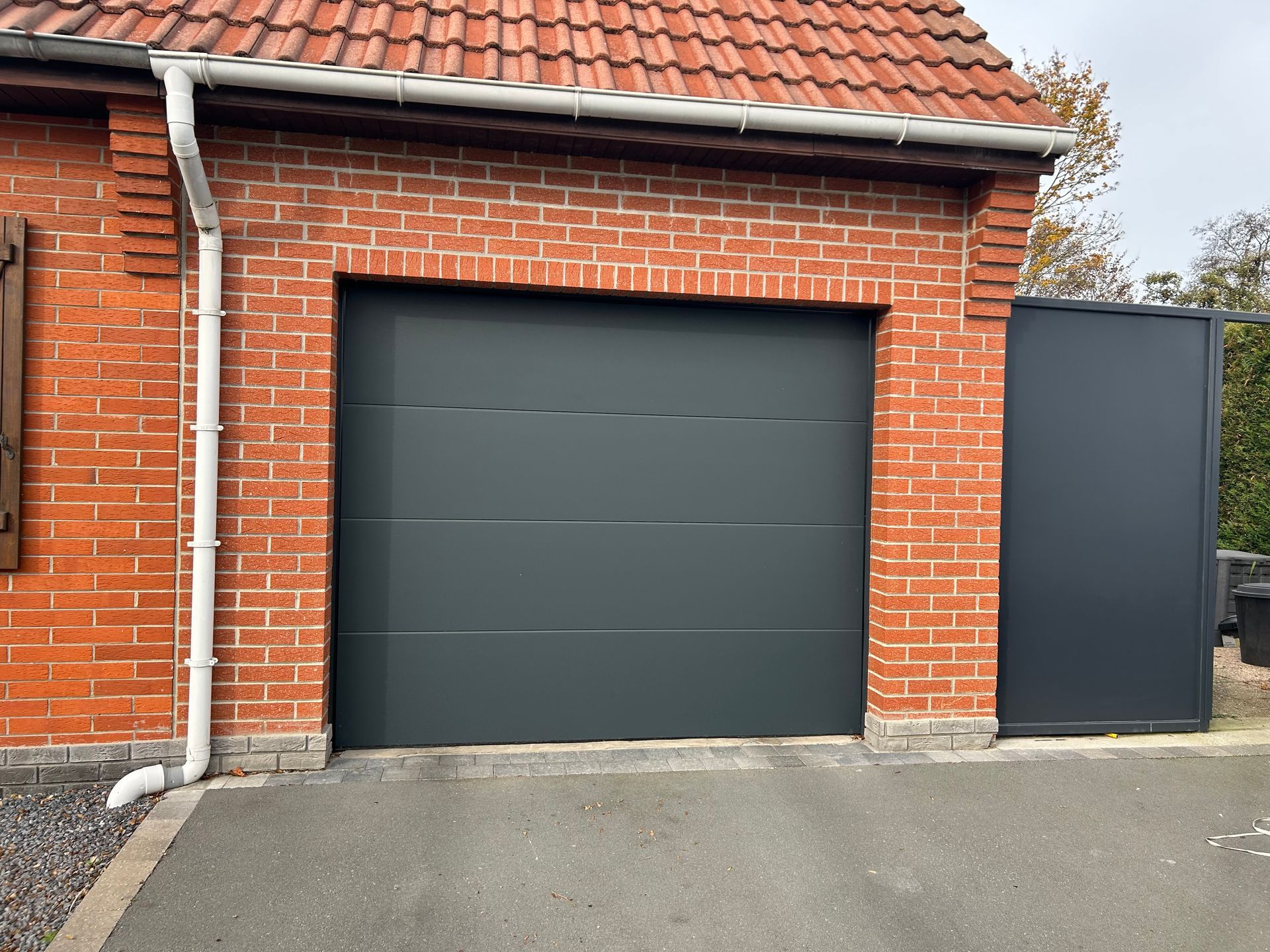 Porte de garage grise encastrée dans un bâtiment en briques rouges.