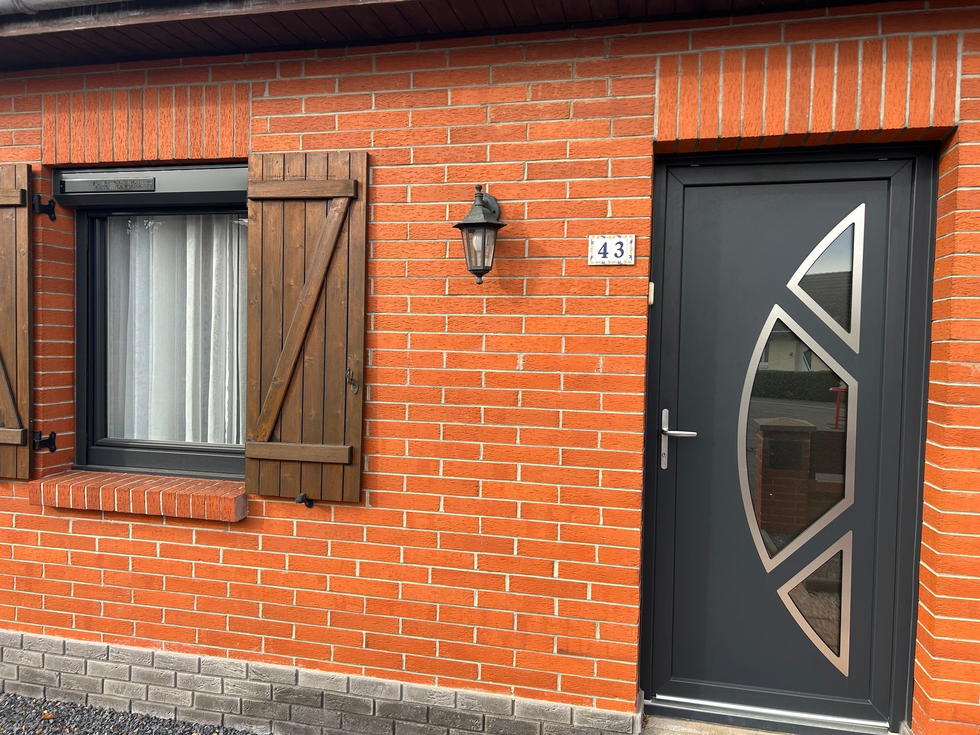 Façade en briques avec porte grise et fenêtre à volets.
