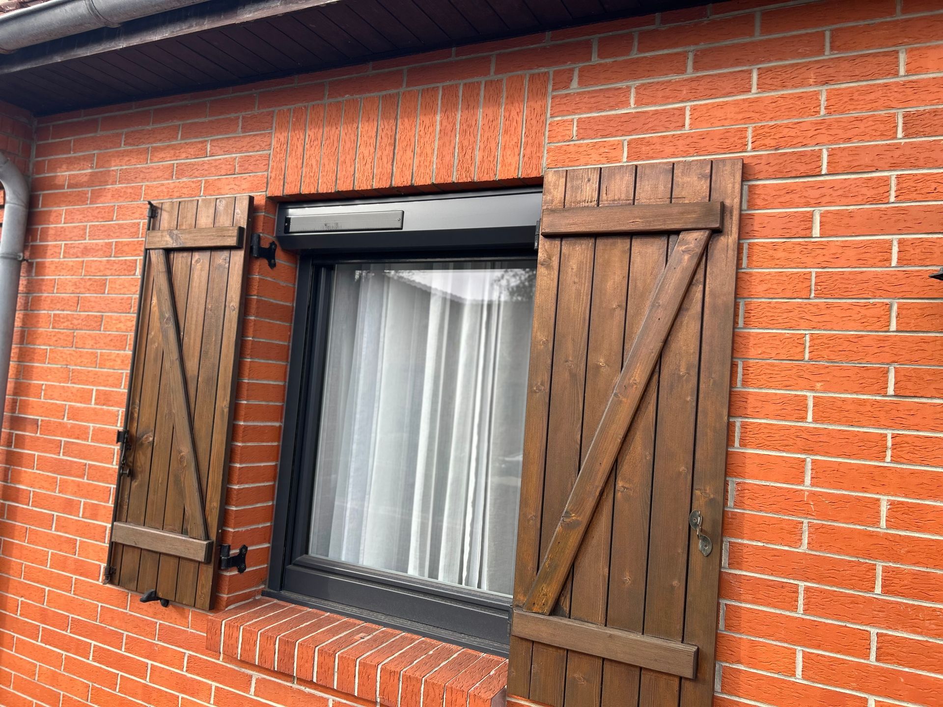 Fenêtre à volets en bois sur un bâtiment en briques.