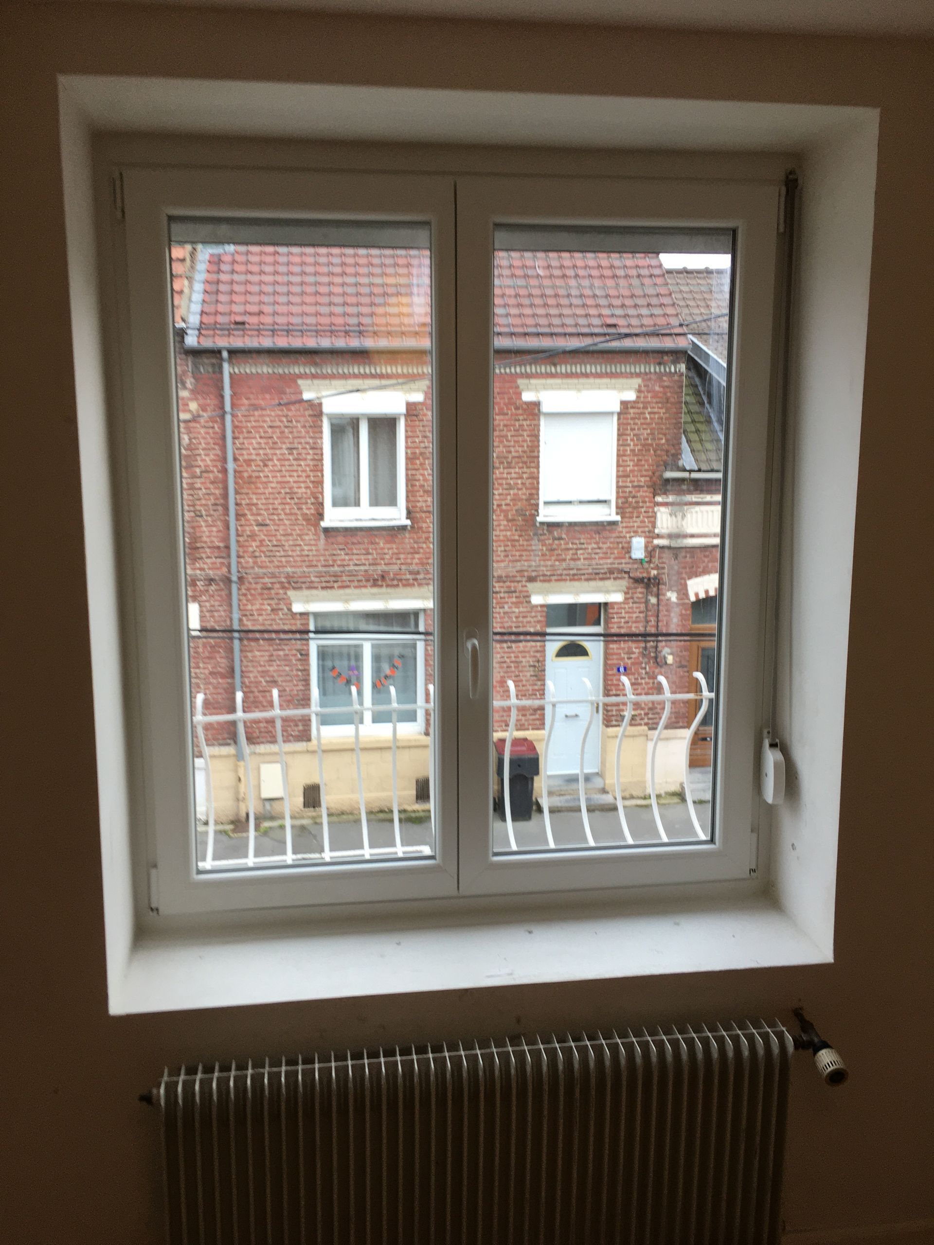 Fenêtre blanche donnant sur un bâtiment en briques.