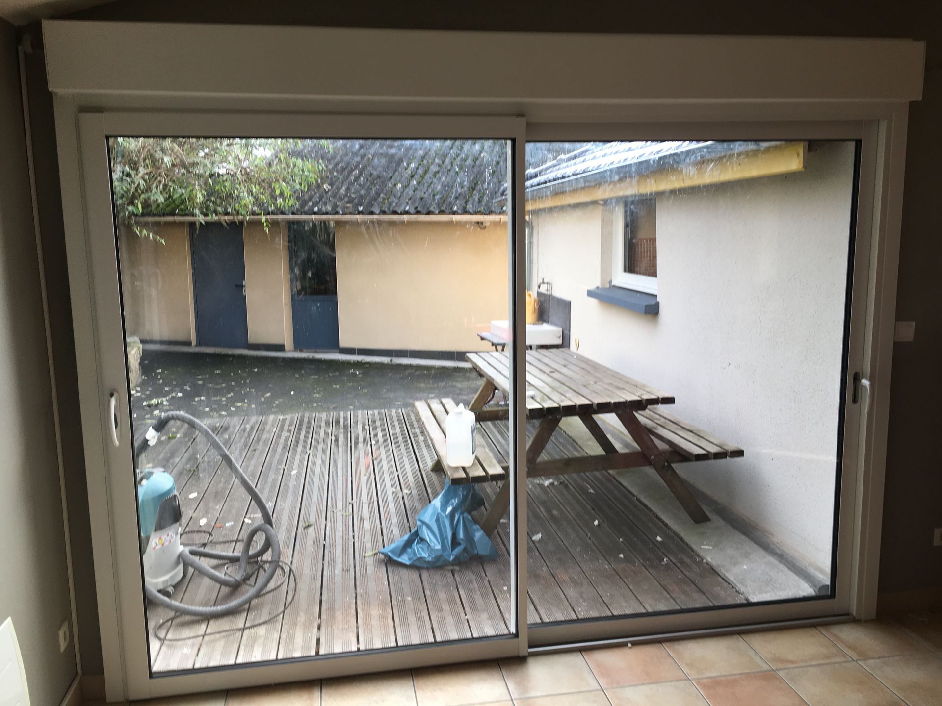Une baie vitrée coulissante en verre donnant sur une terrasse en bois avec une table de pique-nique.