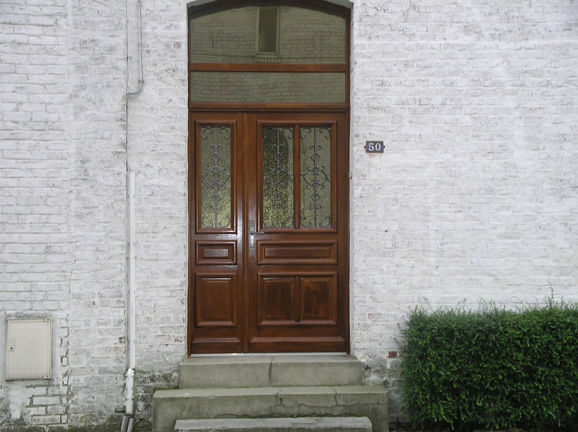 Porte en bois avec imposte dans un mur de briques blanches.
