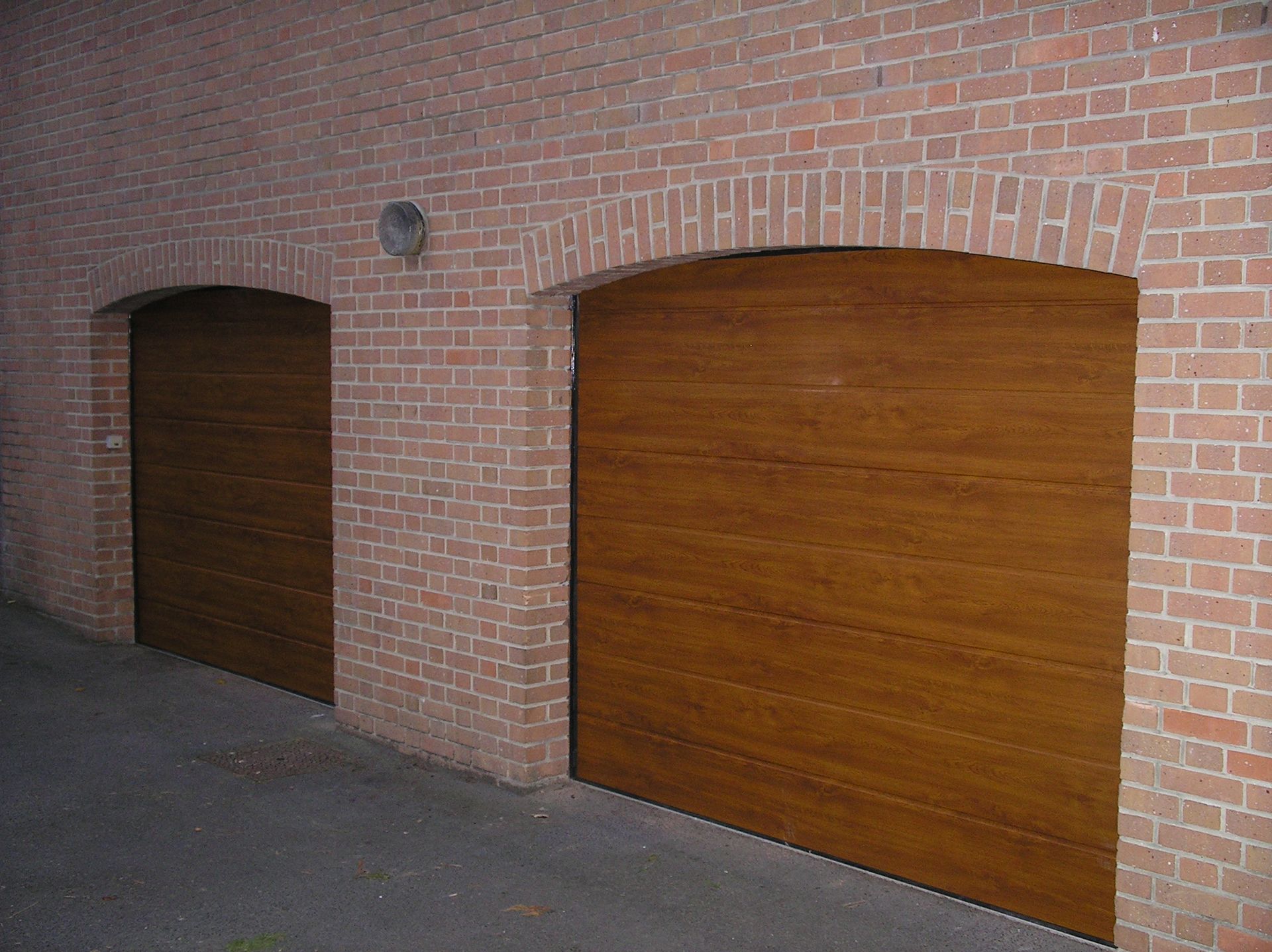 Deux portes de garage à panneaux de bois encastrées dans des arcades en briques.