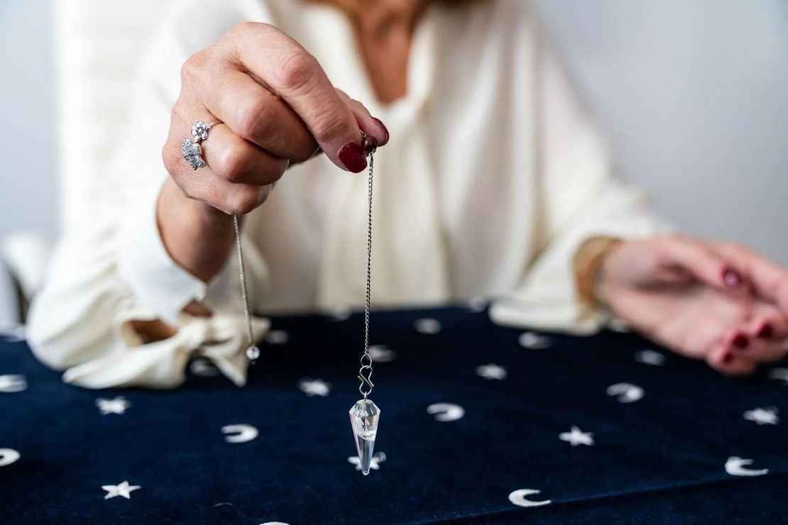 Des mains tenant un pendule en cristal au-dessus d'un tissu à motifs d'étoiles