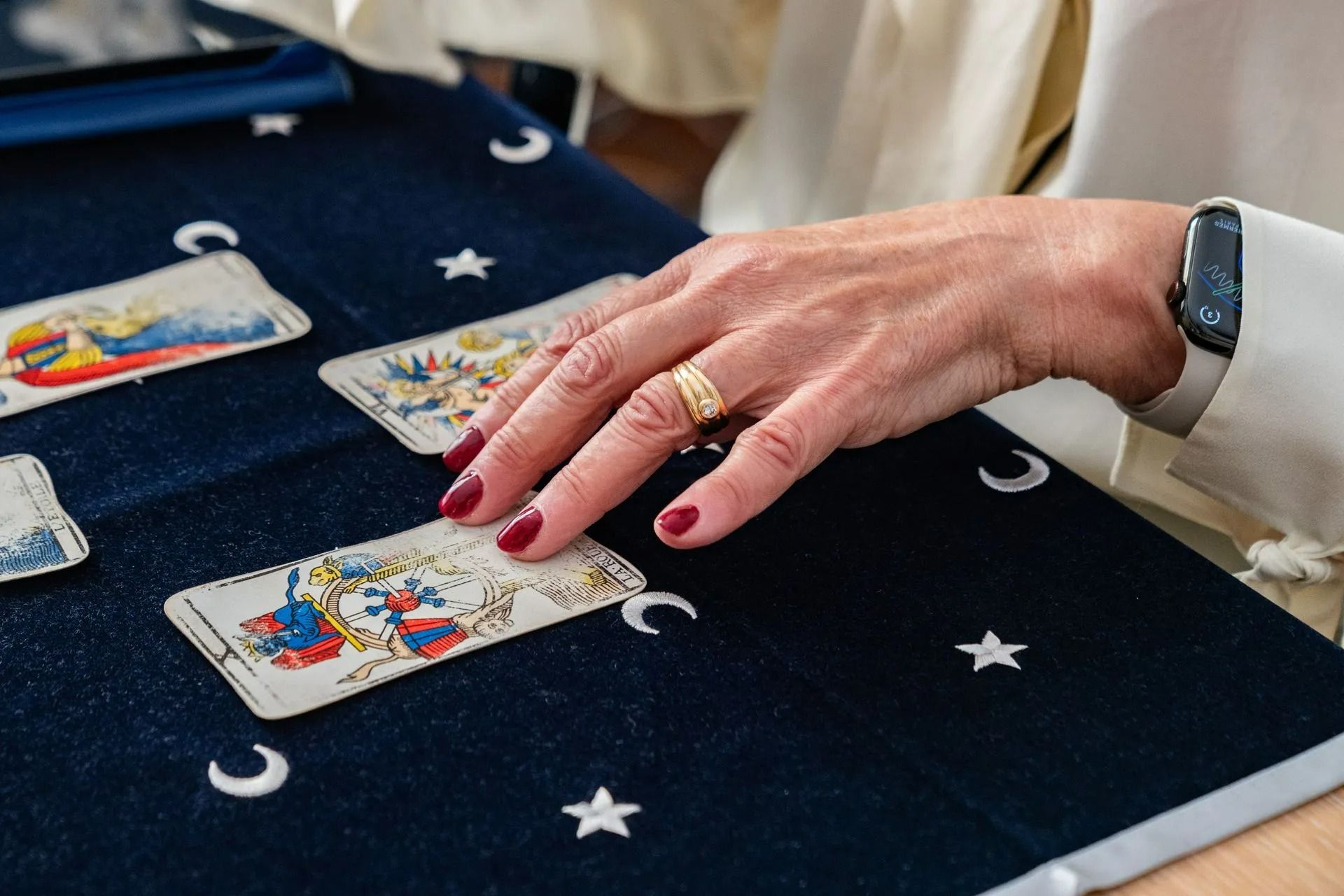 Une main distribuant des cartes de tarot sur un tissu bleu marine étoilé, avec du vernis à ongles rouge et une bague visibles