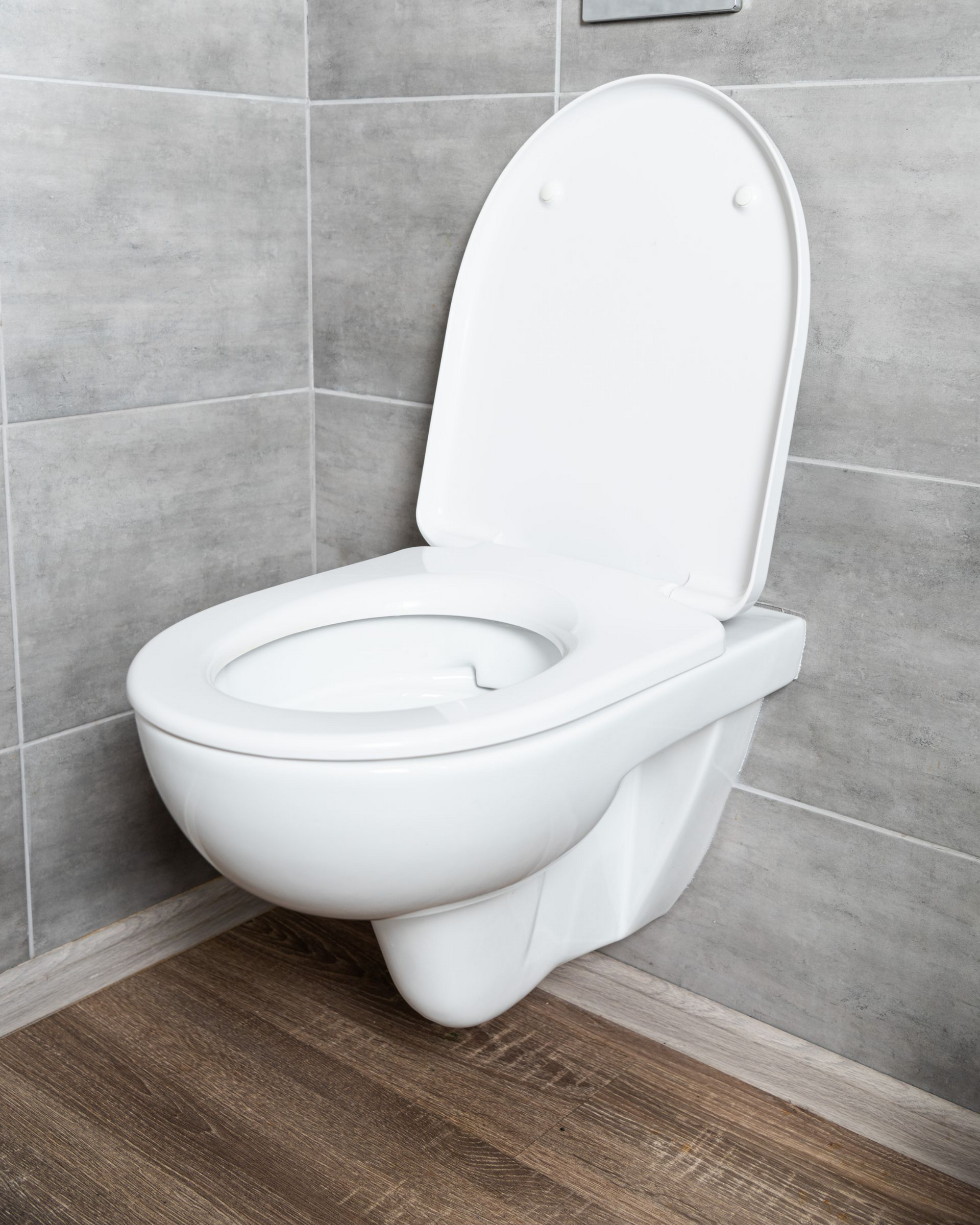 Toilettes blanches suspendues, abattant relevé. Mur carrelé gris et sol imitation bois.