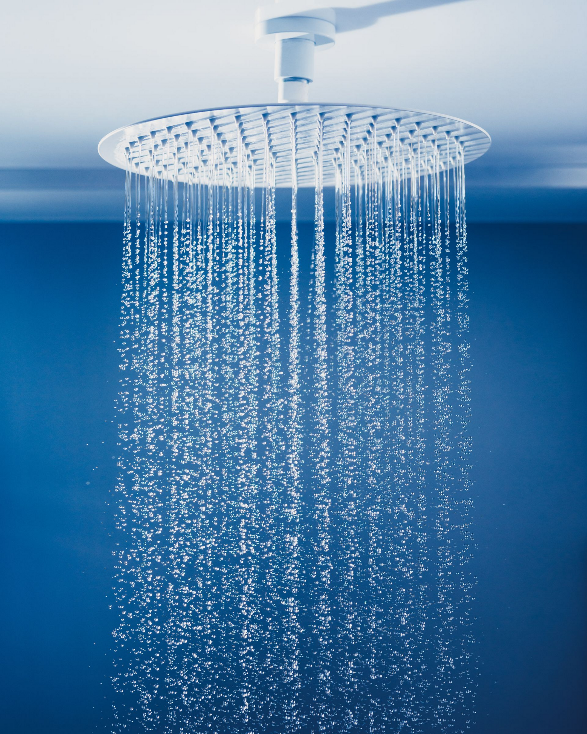 Pommeau de douche de tête en fonctionnement. Robinet blanc sur fond bleu.