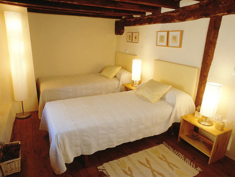 Dormitorio con dos camas individuales, ropa de cama blanca, vigas de madera, lámparas y una pequeña alfombra.