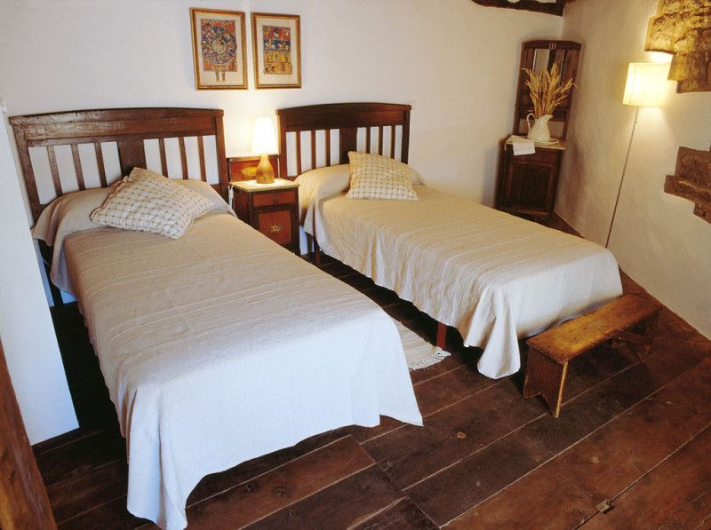 Dos camas individuales en un dormitorio rústico con suelos y cabeceros de madera, mesitas de noche y obras de arte.