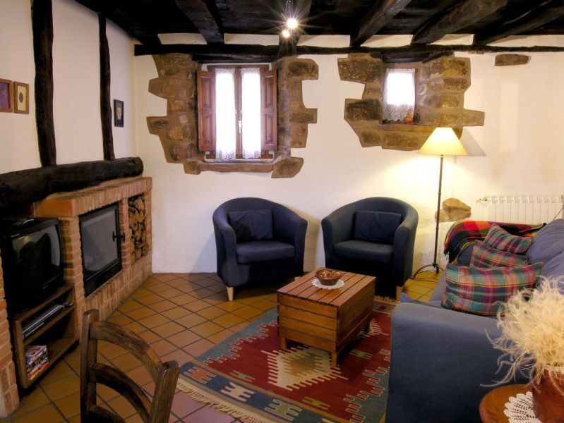 Acogedora sala de estar con chimenea de ladrillo, vigas a la vista, sillones azules y una alfombra estampada.