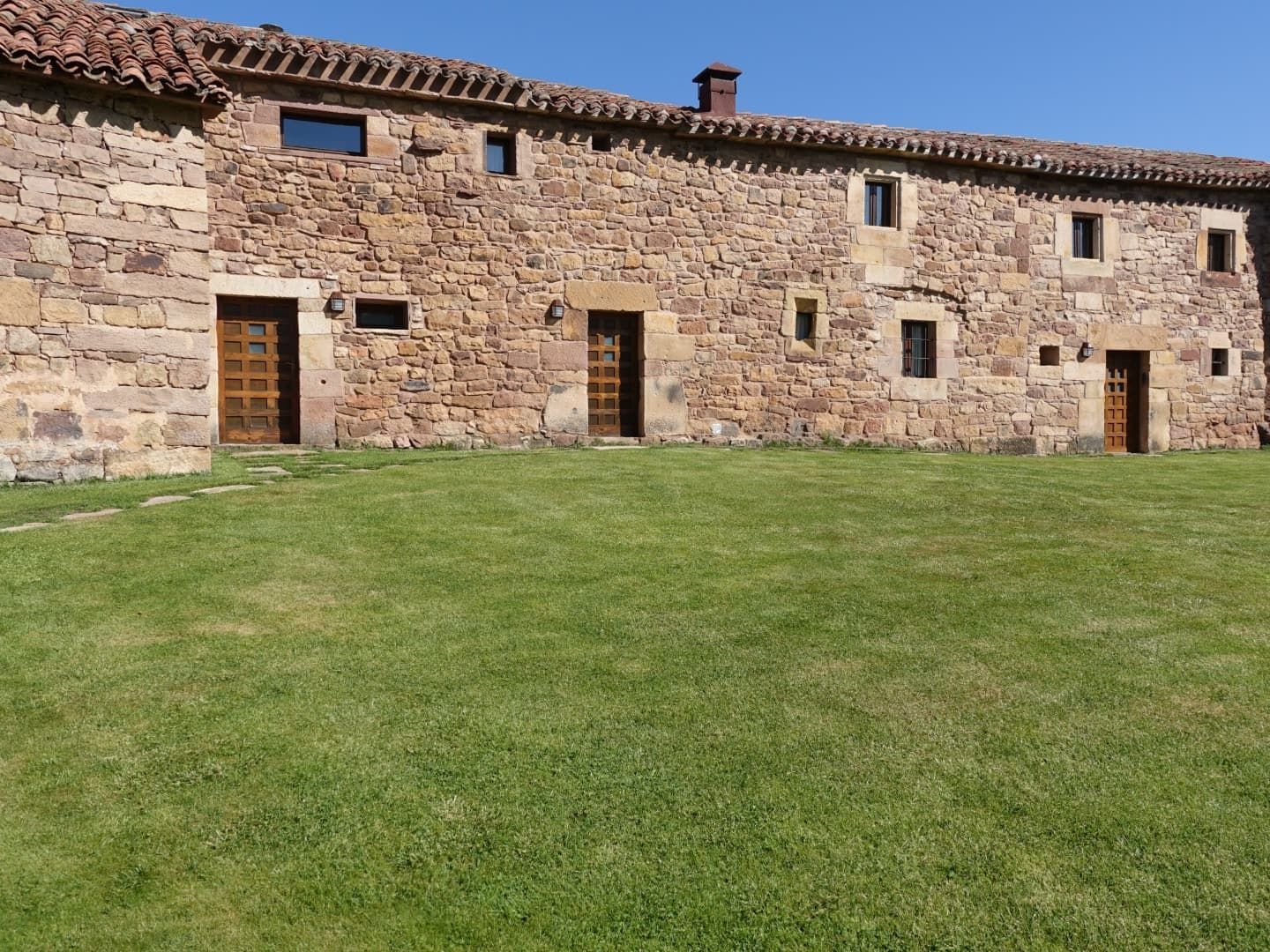 Edificio de piedra con múltiples puertas y ventanas, frente a un césped y un cielo azul claro.