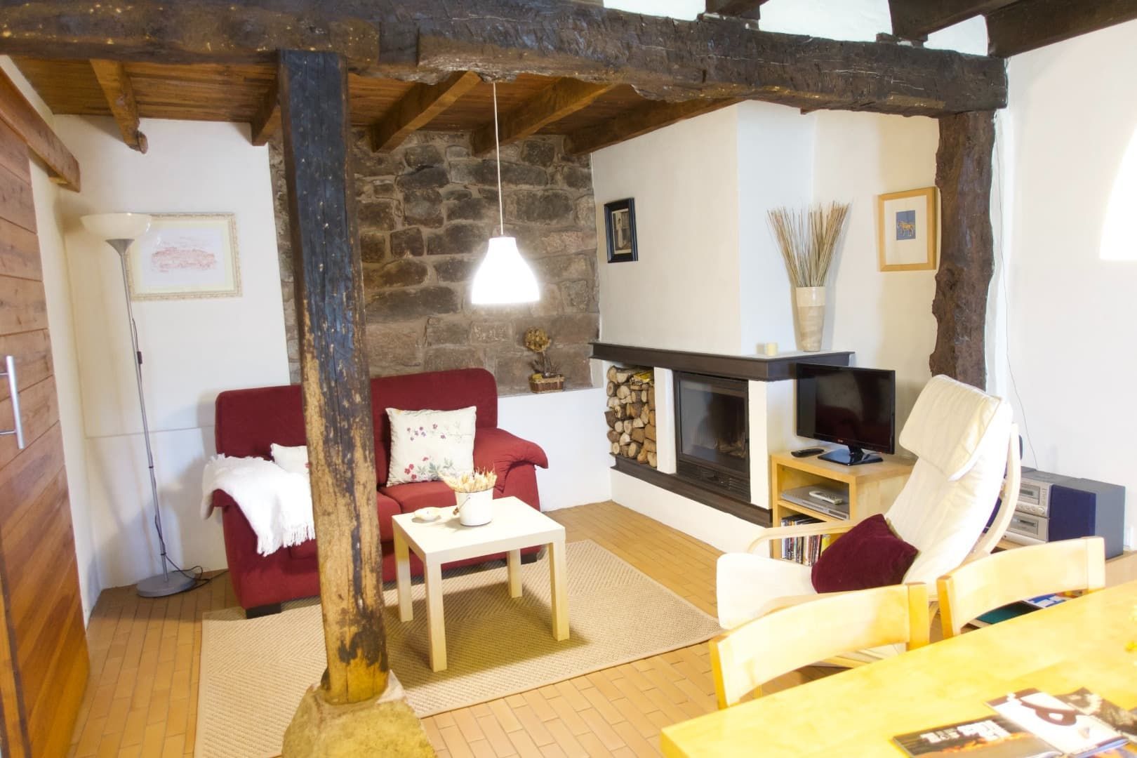 Acogedora sala de estar con chimenea, vigas a la vista y sillones rojos.