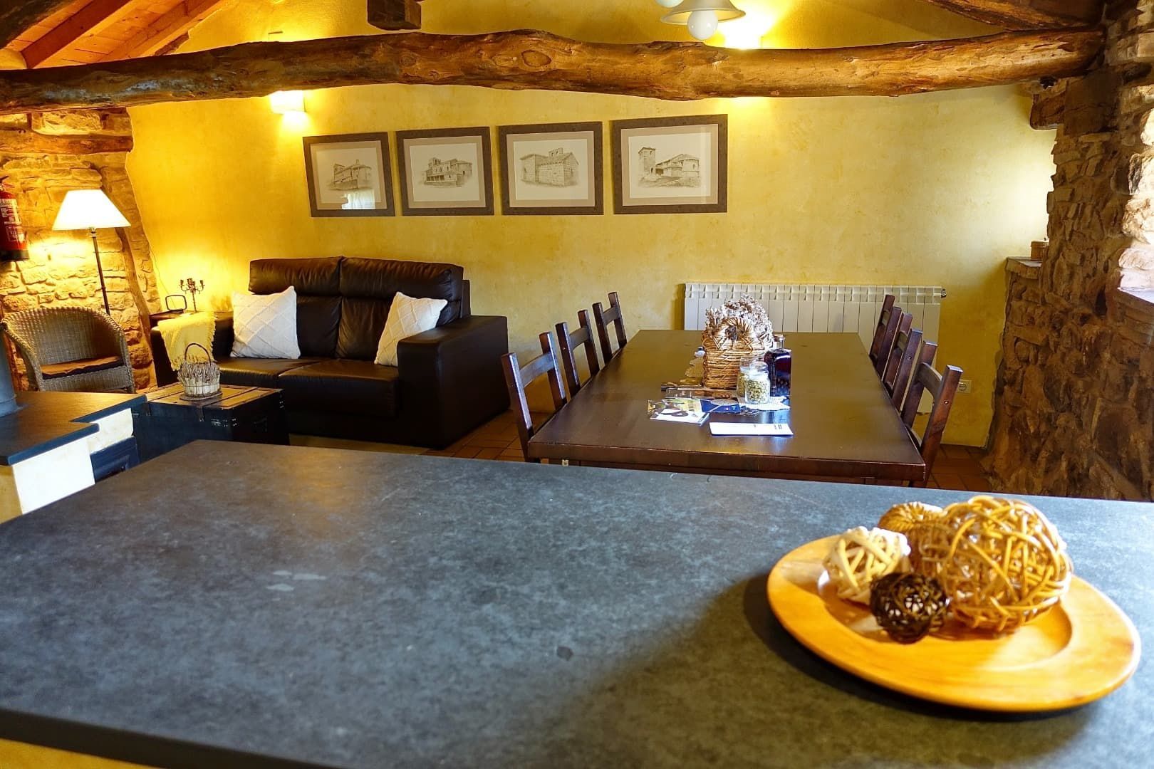 Interior con encimera de cocina, sofá, mesa de comedor y pared de piedra; iluminación cálida.