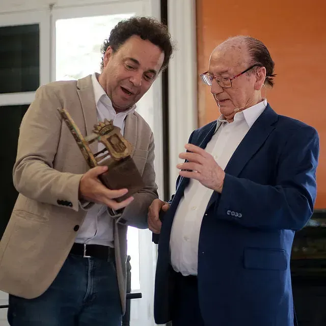 Dos hombres están parados uno al lado del otro y uno sostiene un trofeo.