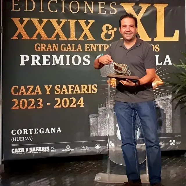 Un hombre sostiene un trofeo frente a un cartel que dice ediciones xxxix y xl