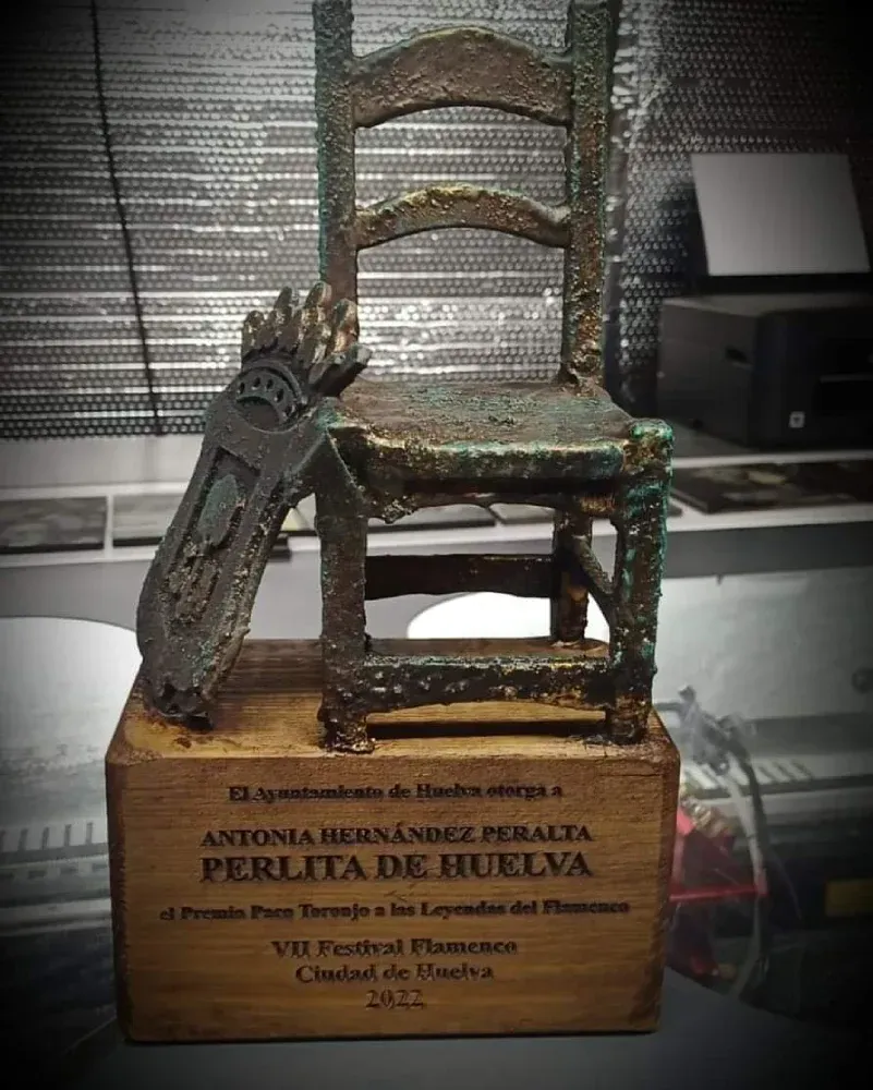 Una estatua de una silla sentada encima de una caja de madera que dice antonia hernandez peralta perlita de huelva