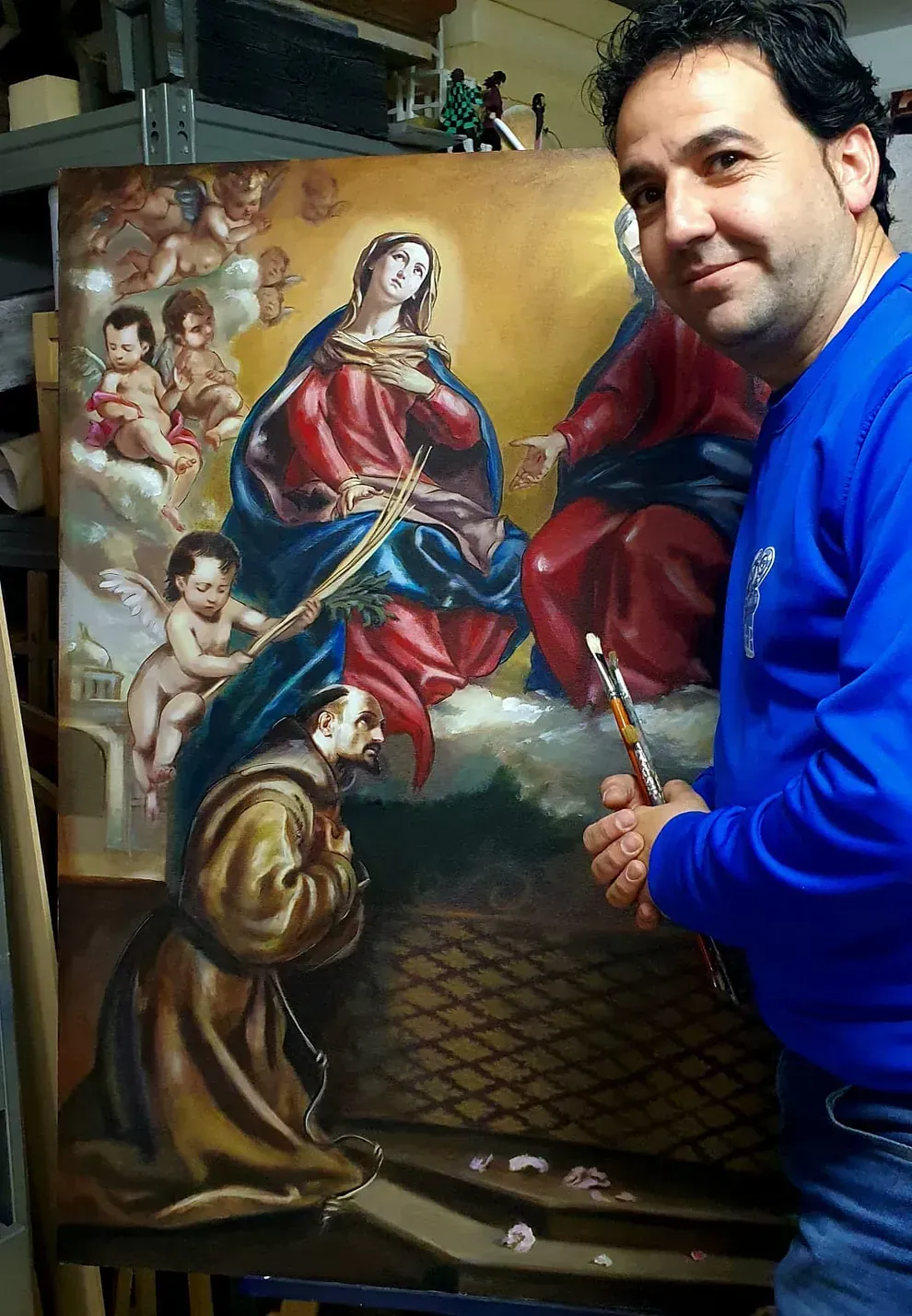Un hombre con una camisa azul está pintando un cuadro de Jesús y María.