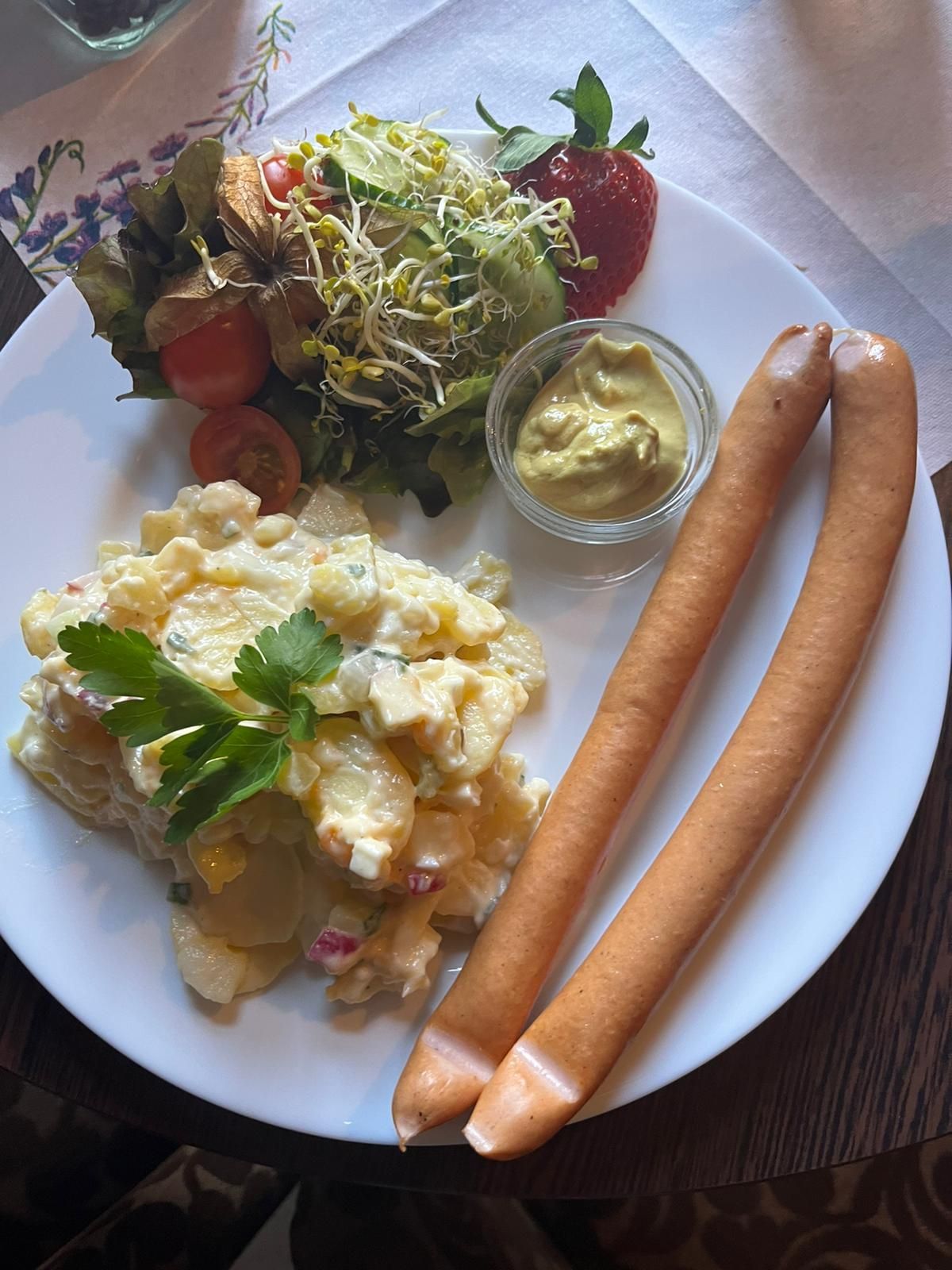 Ein Teller mit Würstchen, Kartoffelsalat und Salat auf einem Tisch.