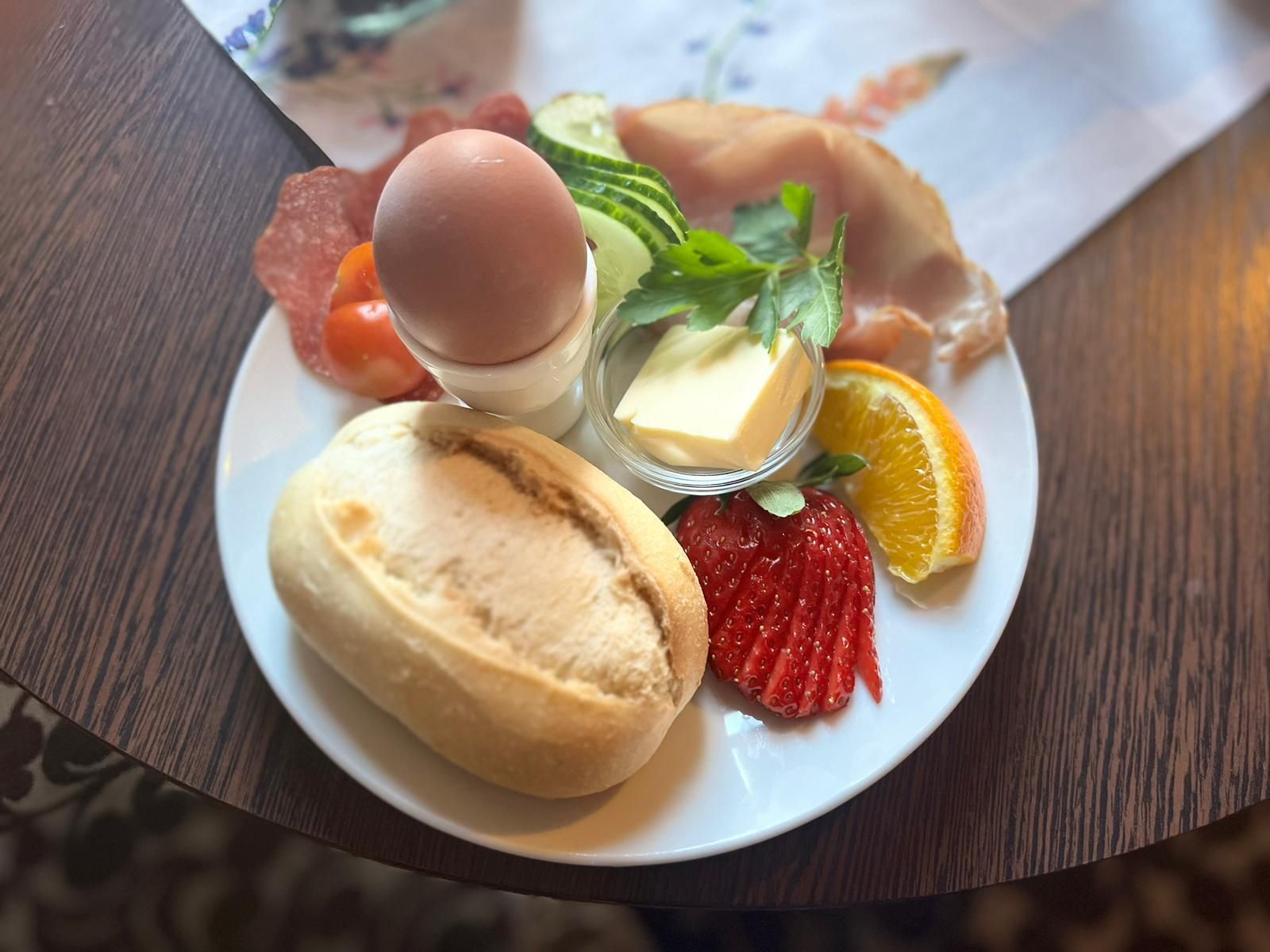 Ein Teller mit Essen, einem Sandwich, Ei, Gemüse und Butter auf einem Tisch.