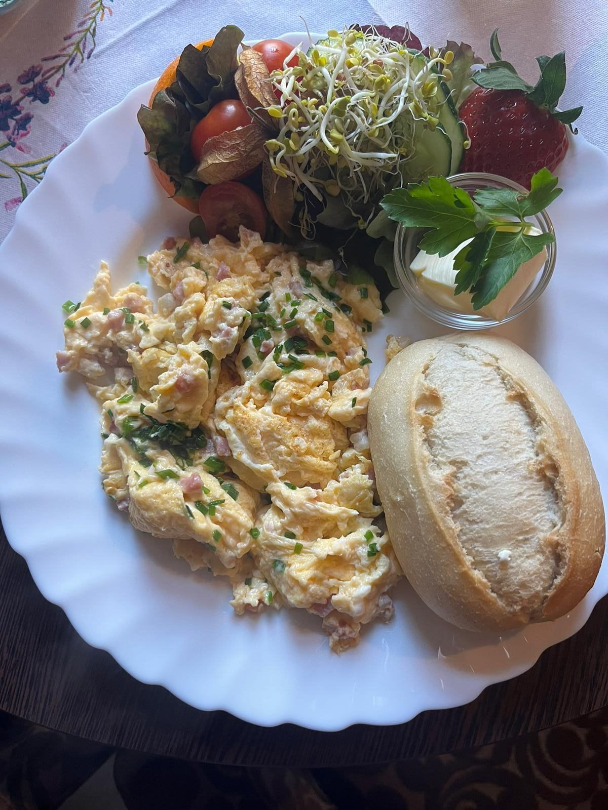 Ein weißer Teller mit Rührei, einem Brötchen und einem Salat.