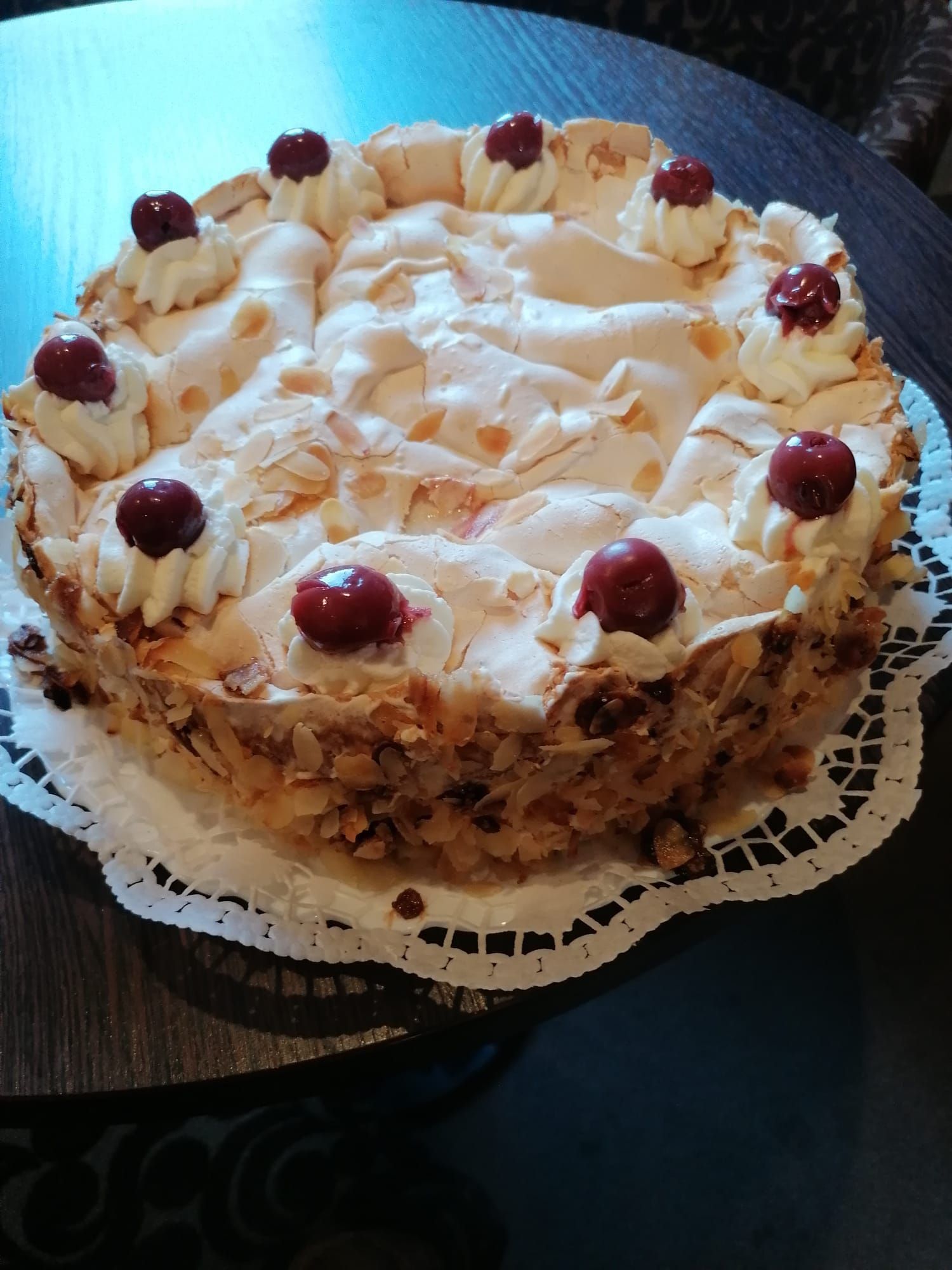 Auf einem Tisch steht ein Kuchen mit Schlagsahne und Kirschen obendrauf.