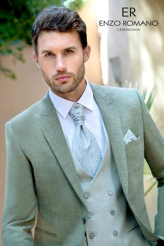 Hombre con traje verde, chaleco, camisa blanca y corbata estampada, al aire libre.