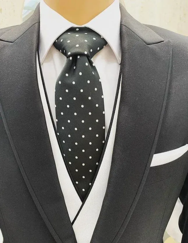 Hombre con traje gris oscuro, camisa blanca, chaleco y corbata de lunares; se ve un pañuelo de bolsillo blanco.