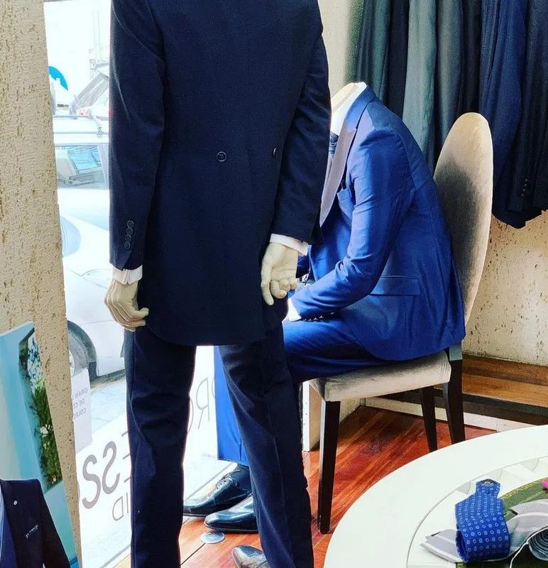 Maniquí con traje azul y abrigo, y otro con traje azul sentado. Exhibido en tienda.