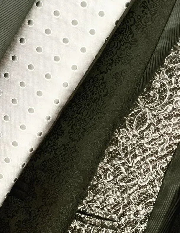 Primer plano de tres telas: una blanca con ojales, una verde oscuro con estampado integral y una negra con encaje floral.