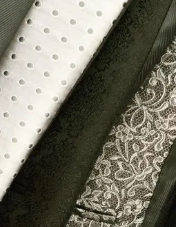 Primer plano de tres telas enrolladas: una blanca con ojales, una verde oscuro con estampado integral y una negra con encaje floral.