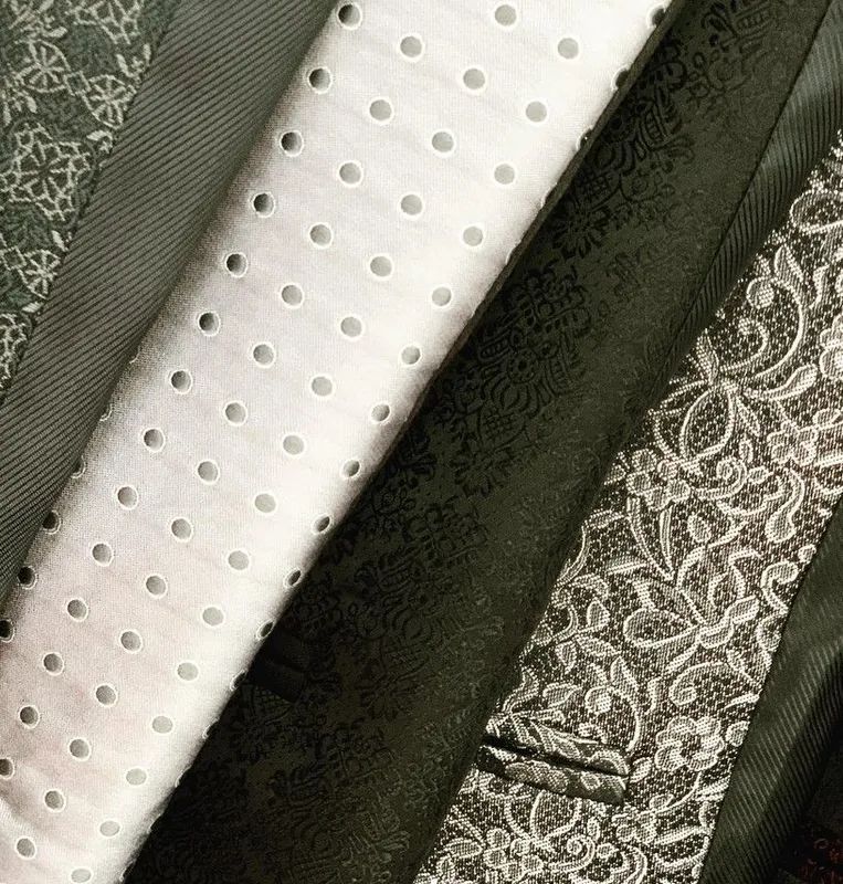 Primer plano de muestras de tela: ojal blanco, verde oscuro y textiles estampados dispuestos en ángulos.