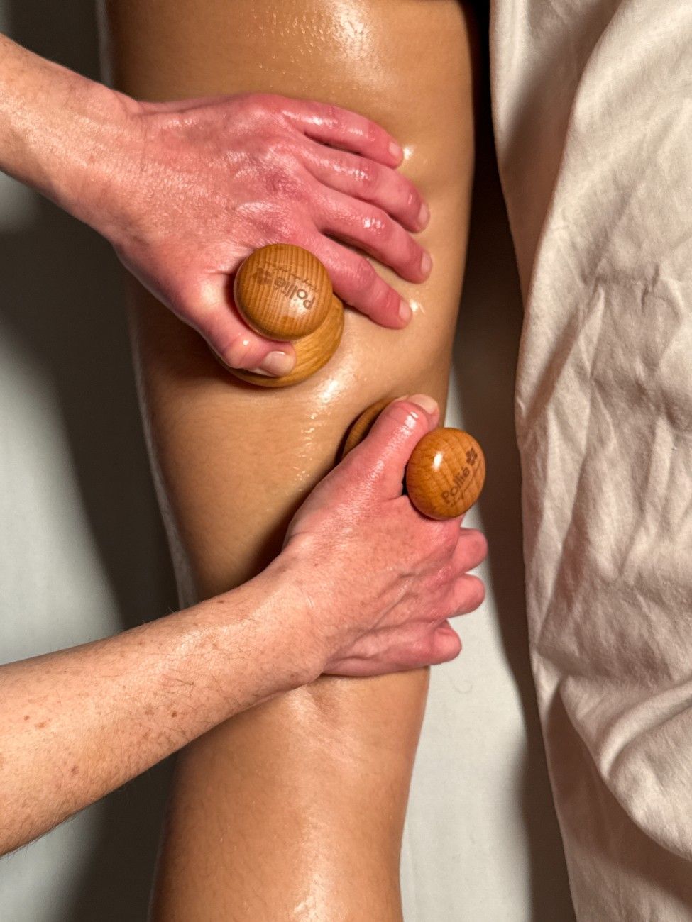Manos masajeando una pierna con herramientas de madera. La pierna está sobre una superficie blanca.