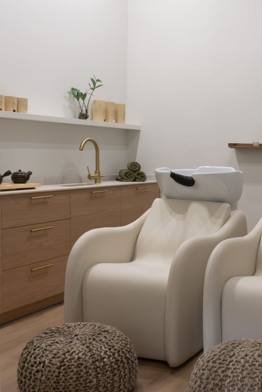 Interior de salón con dos sillas blancas, un lavabo y muebles de madera.