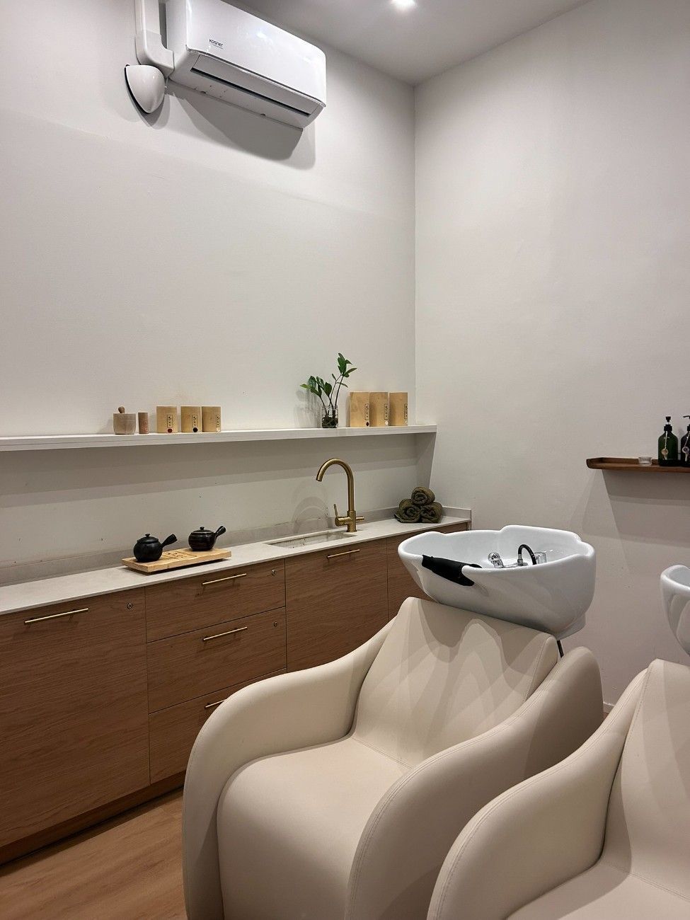 Estación de lavado de cabello de salón con dos sillas beige, lavabo y gabinetes de madera.