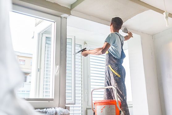 Un hombre está de pie en una escalera pintando el techo de una habitación.