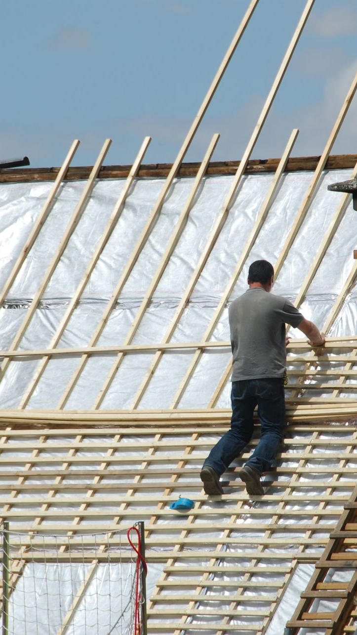 Un ouvrier du bâtiment sur un toit, installant des chevrons en bois. Ciel dégagé.