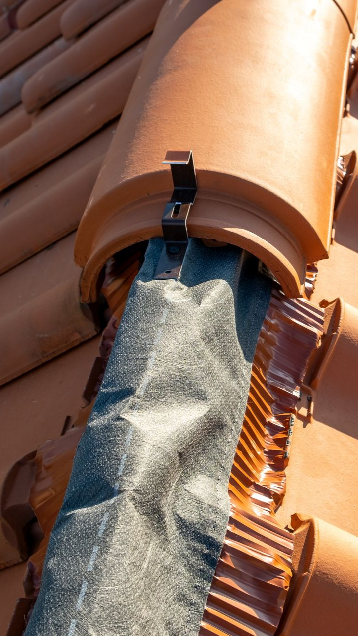 Tuiles de toit en terre cuite avec une grille de protection de gouttière noire maintenue en place par des clips métalliques.