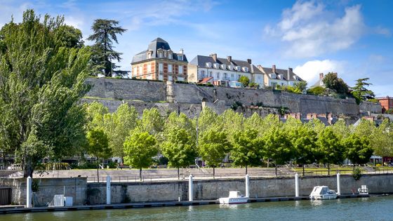 Cours d'eau en premier plan avec des bateaux amarrés le long d'un muret, en second plan se trouve de grosses maisons entourées d'arbres
