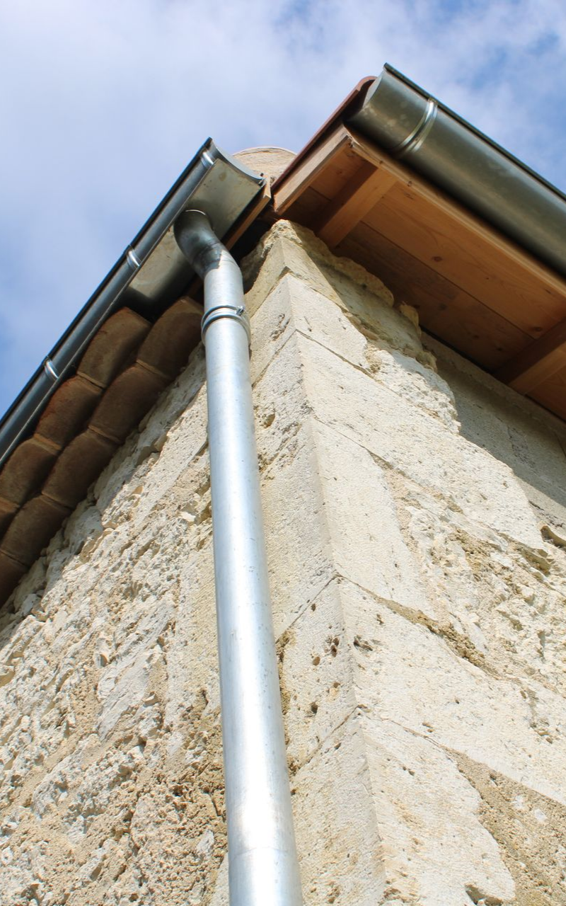 Coin d'un bâtiment avec une gouttière et une descente pluviale en métal sur fond de ciel bleu.