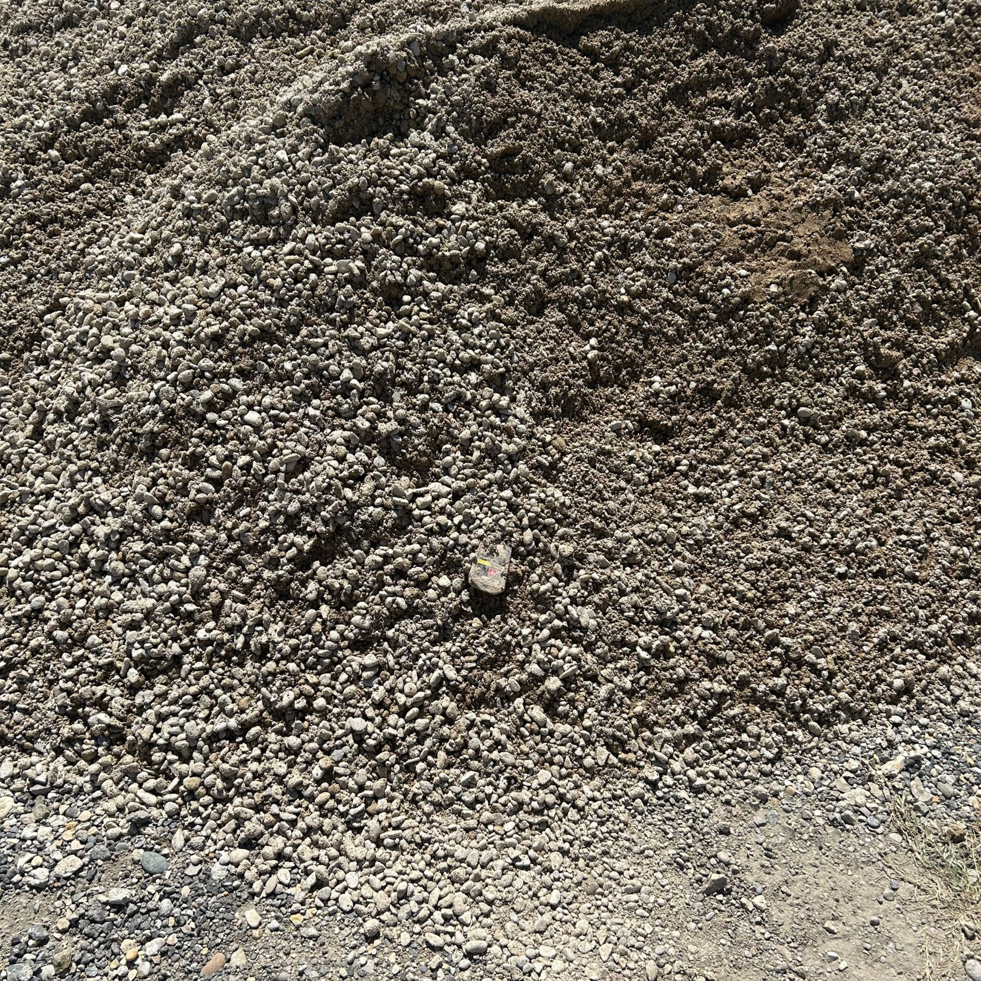 Tas de gravier, de nuances variées de gris et de brun, sur une surface sablonneuse.