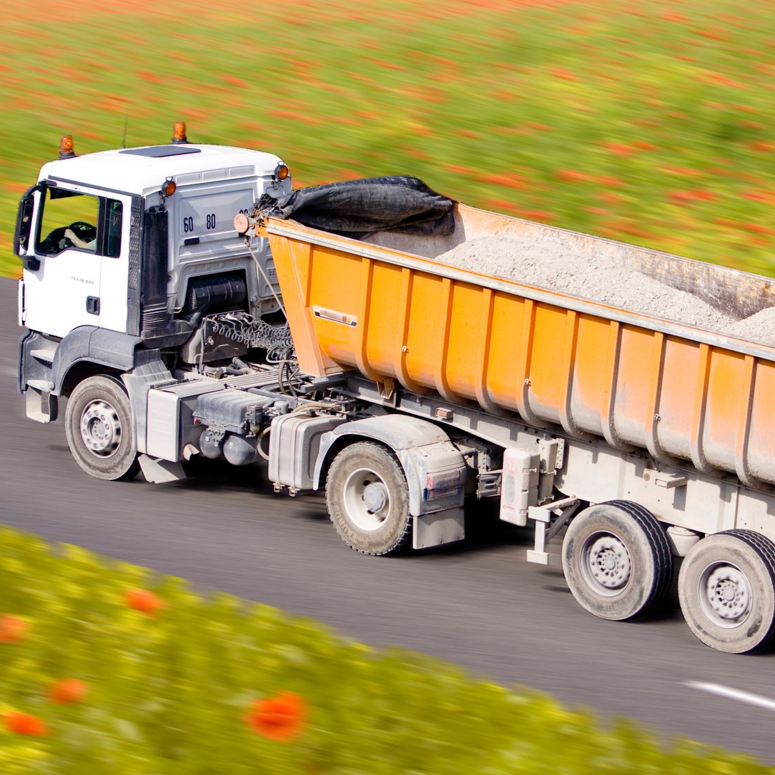 Un camion-benne orange transportant du gravier circule sur une route.