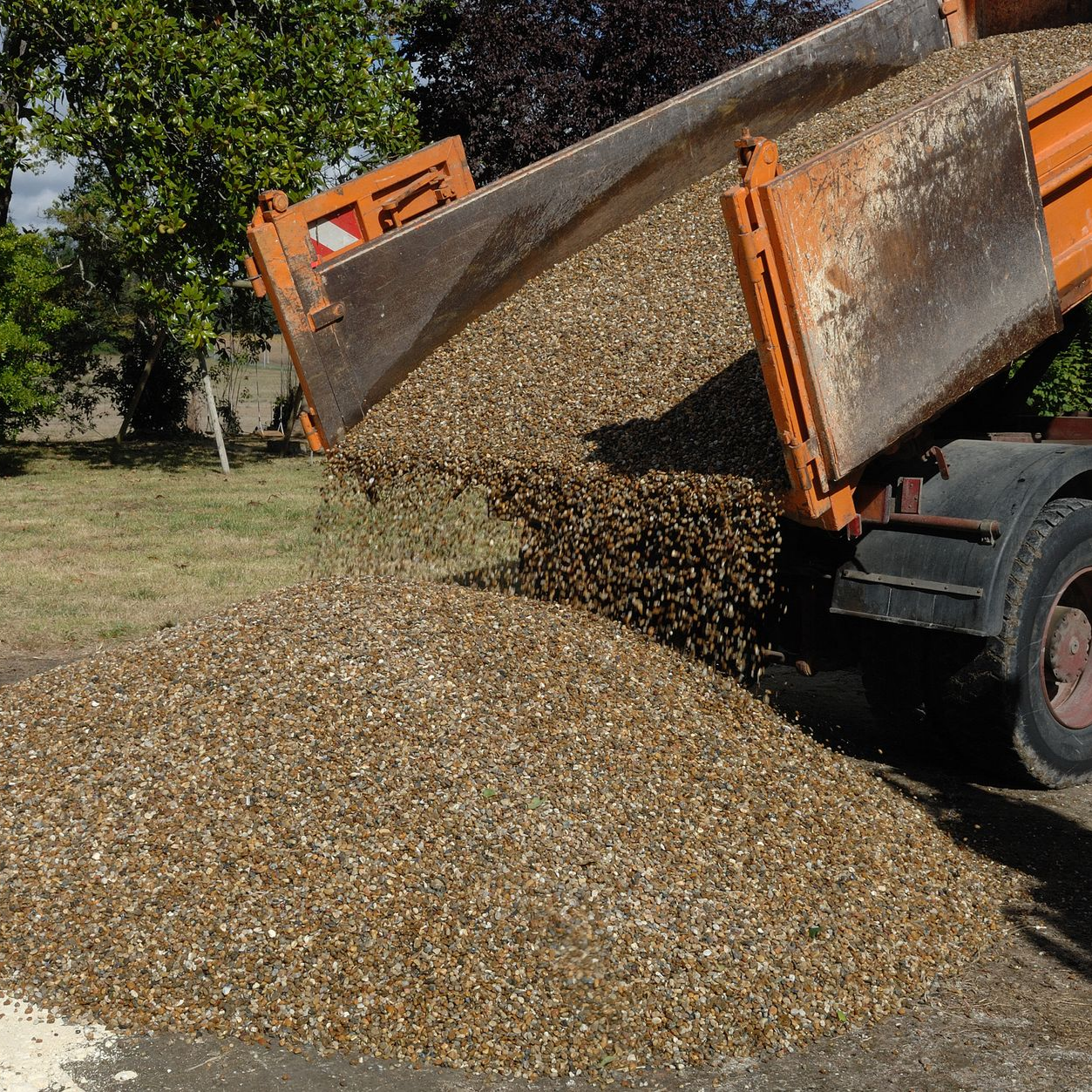 Un camion déchargeant du gravier sur une surface pavée, benne orange.